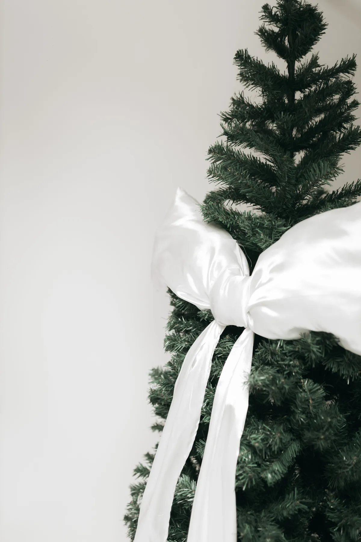 A beautifully adorned Christmas tree with a large white satin bow, perfect for holiday decor.