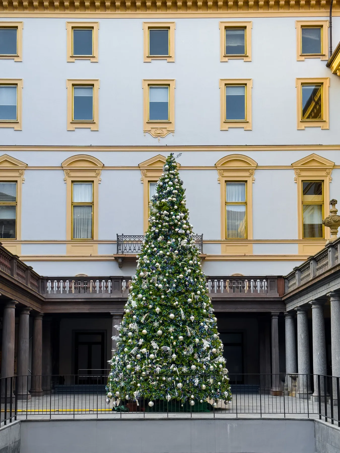 A beautifully decorated Christmas tree in a stylish urban courtyard, framed by classic architecture.