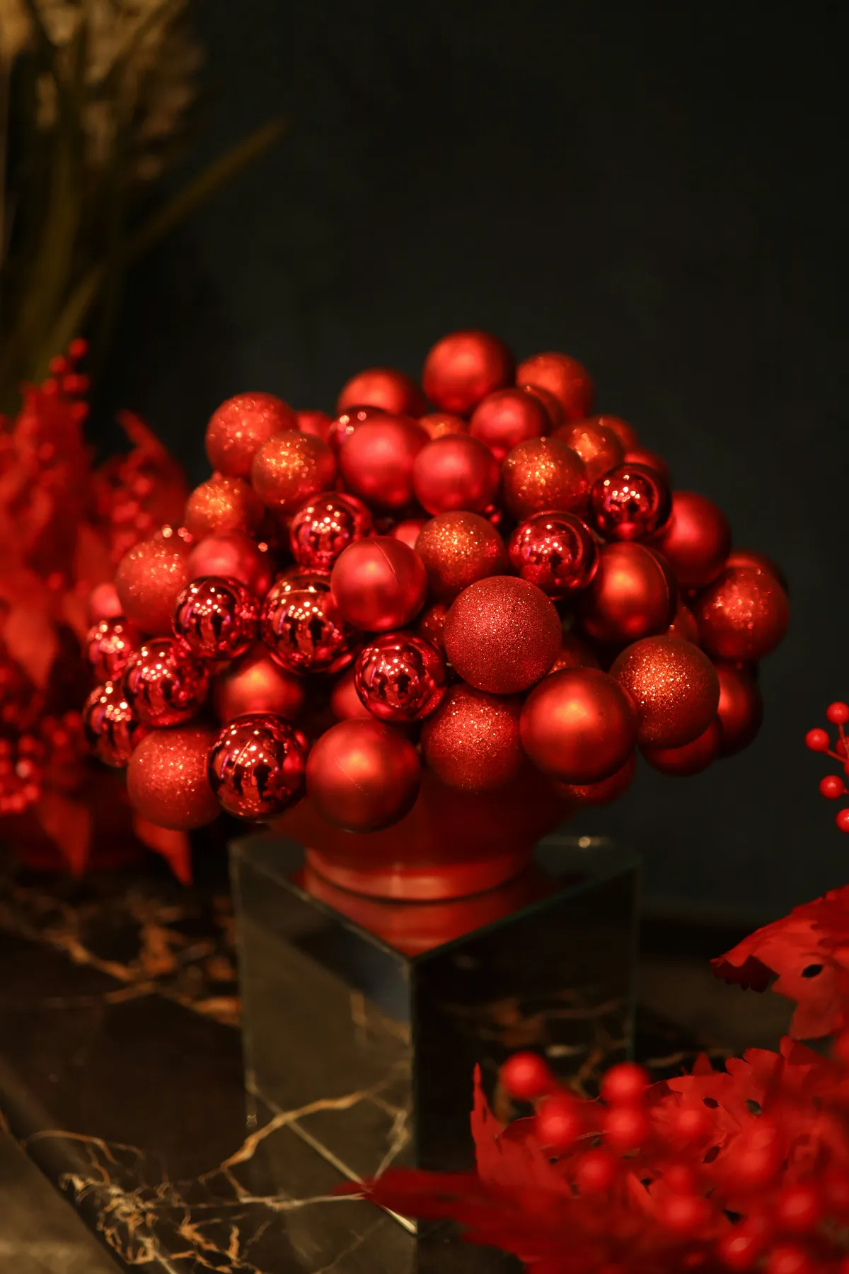 A bold holiday centerpiece made of glossy red ornaments, stacked like a modern bouquet. Sparkle meets minimalism as warm light bounces off matte and metallic textures, creating a festive pop against a