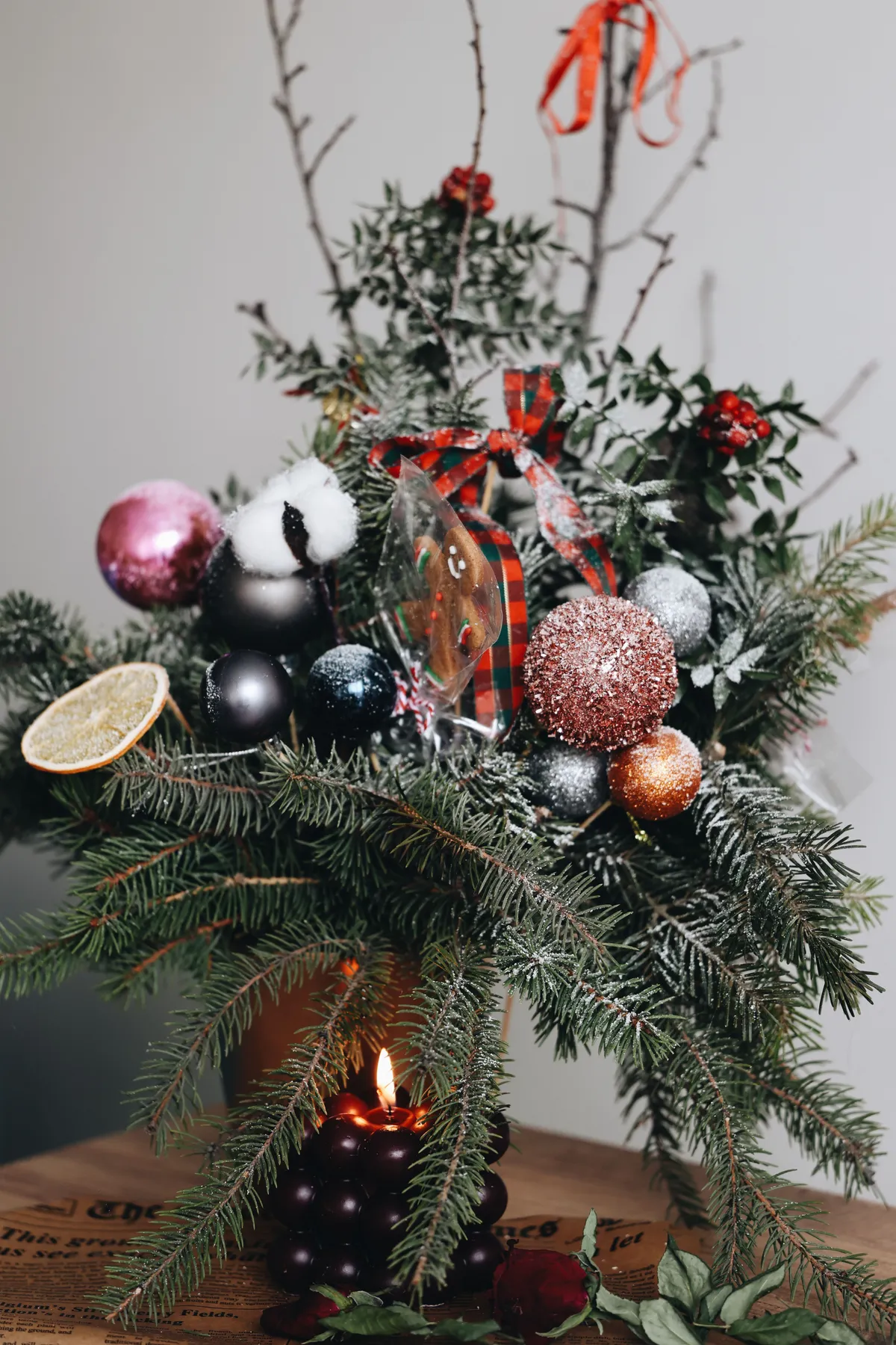 A cozy holiday arrangement featuring pine branches, ornaments, and a candle flame.