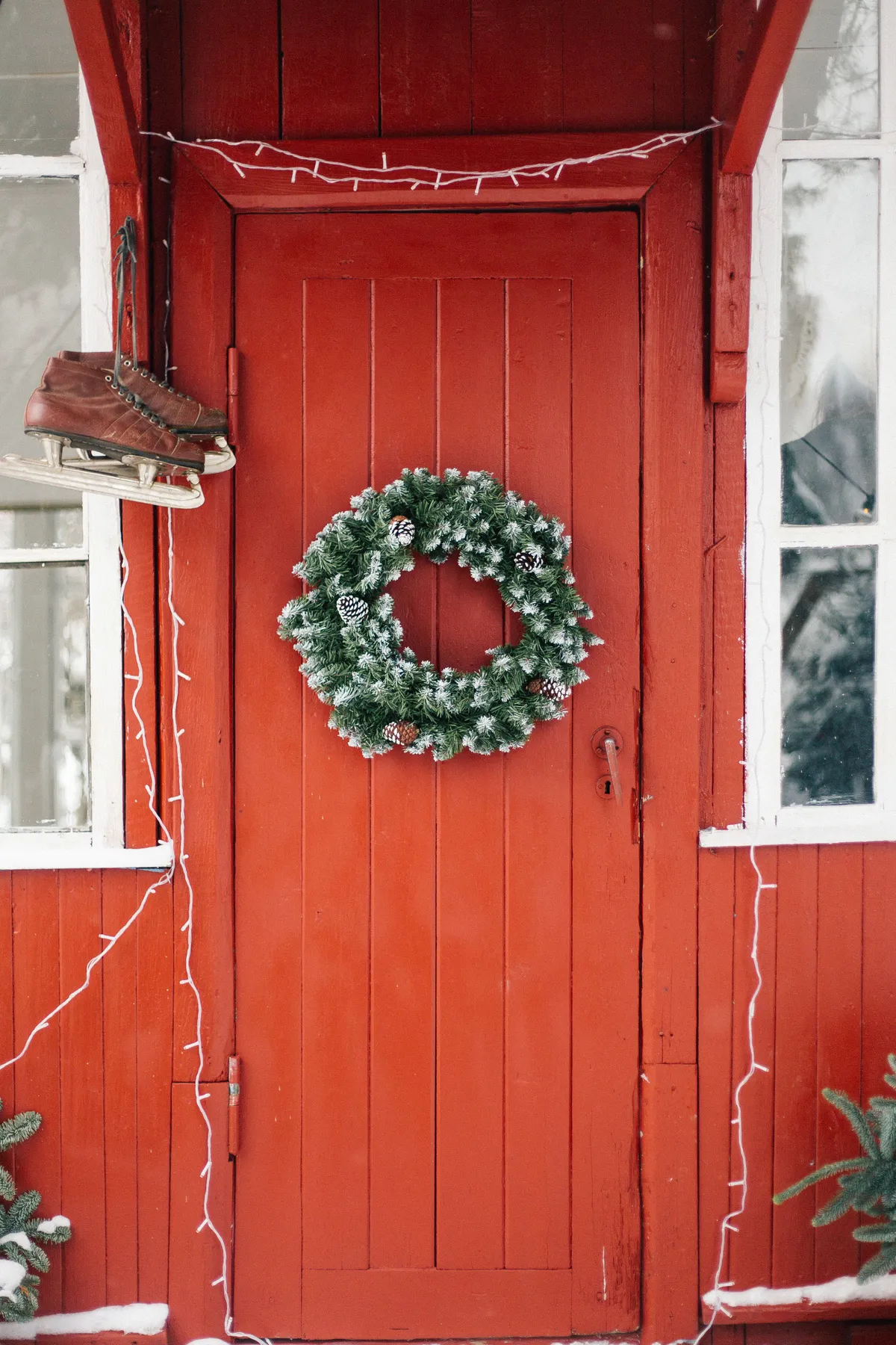 A cozy red wooden door with a green wreath and ice skates, perfect for winter holiday vibes.