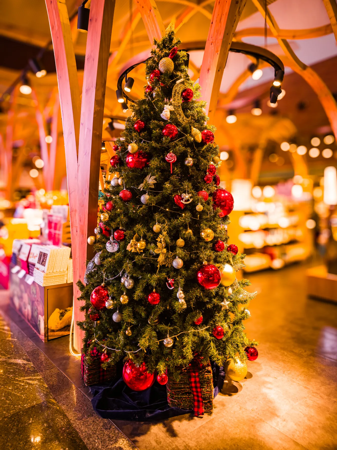 A festive Christmas tree adorned with red and silver ornaments in a shopping mall.