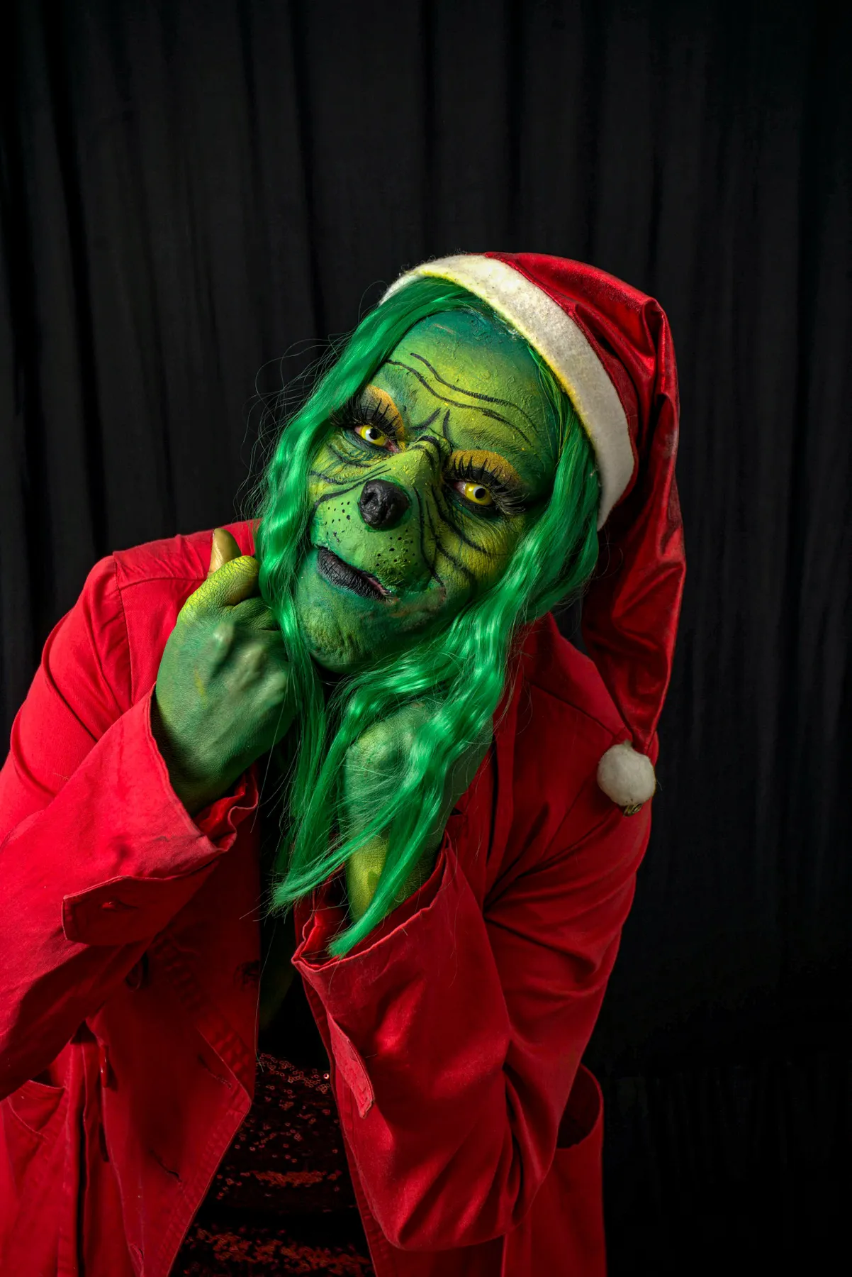 A person dressed as the Grinch with green face paint and Santa costume.