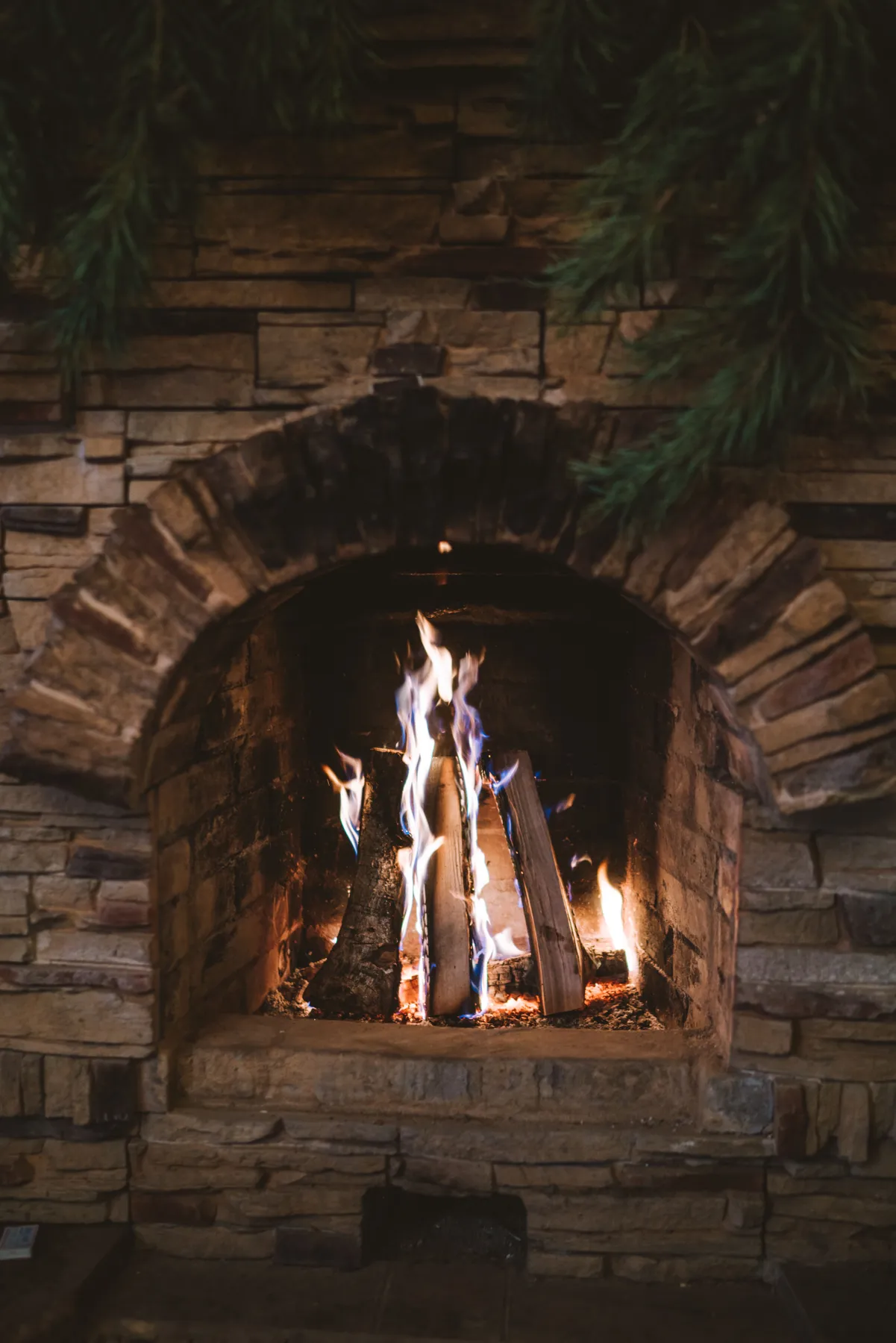 A rustic stone fireplace with logs burning brightly, creating a warm and cozy atmosphere.