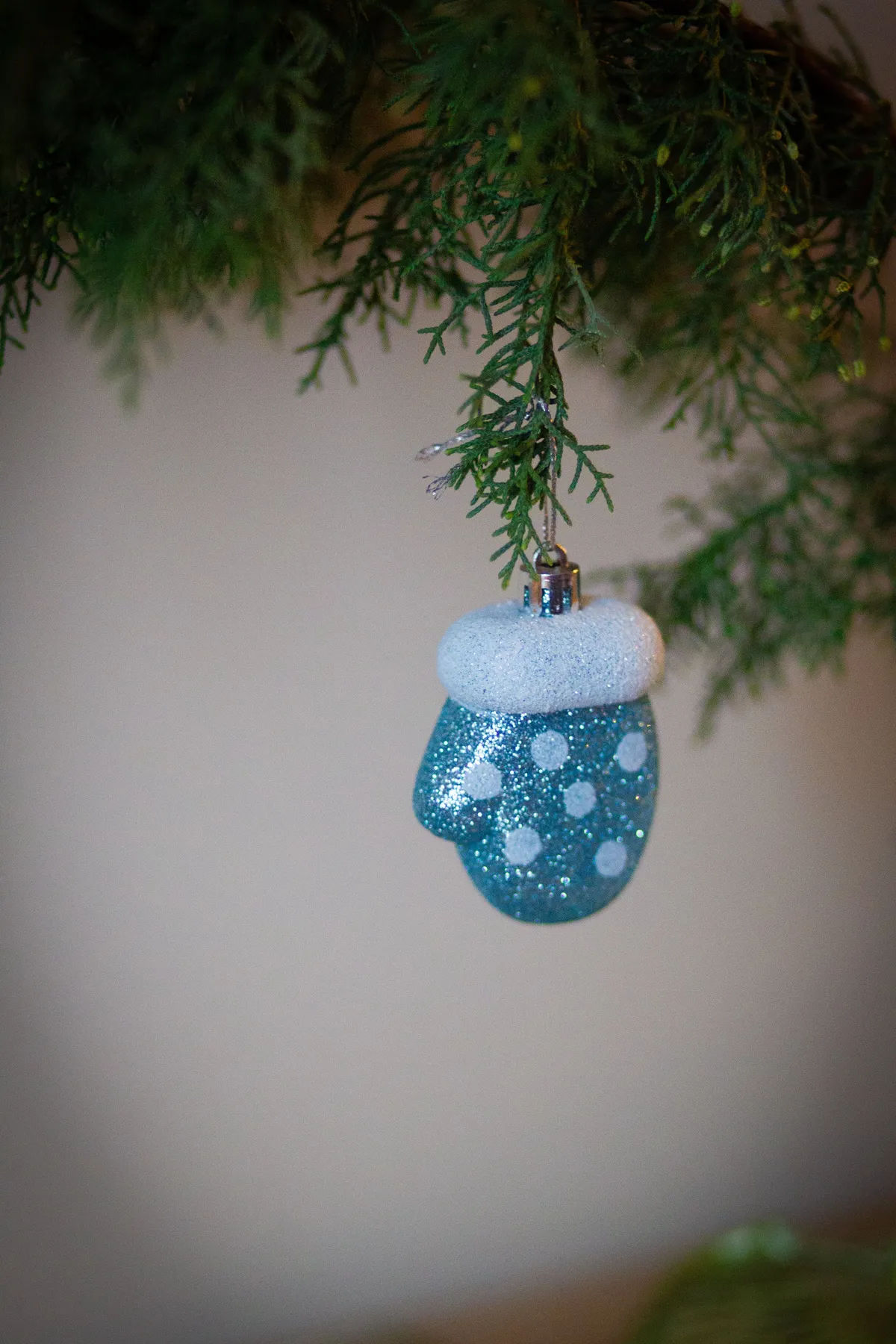 A sparkling blue mitten ornament hanging from a Christmas tree branch.