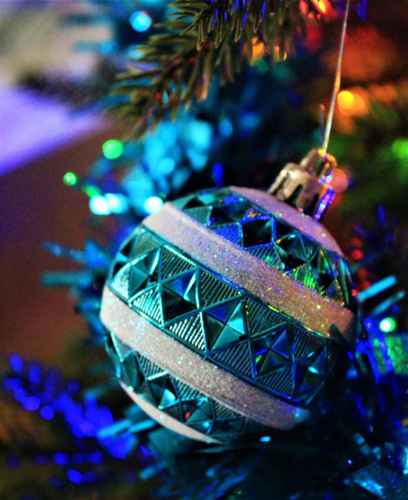 A striking blue Christmas ornament hanging on a tree, surrounded by sparkling lights.