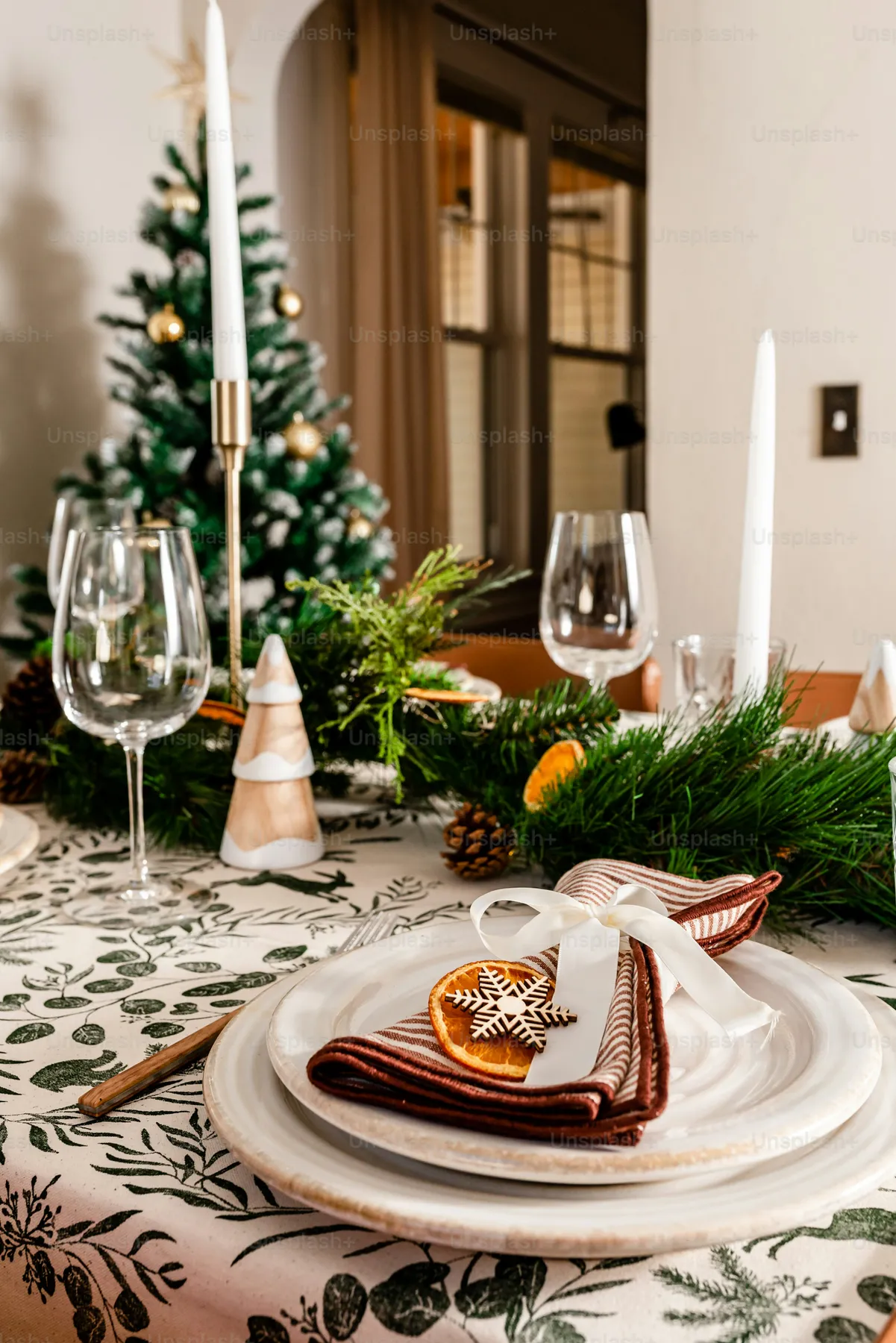 A table set for christmas with a christmas tree in the background - Photo  on Unsplash+