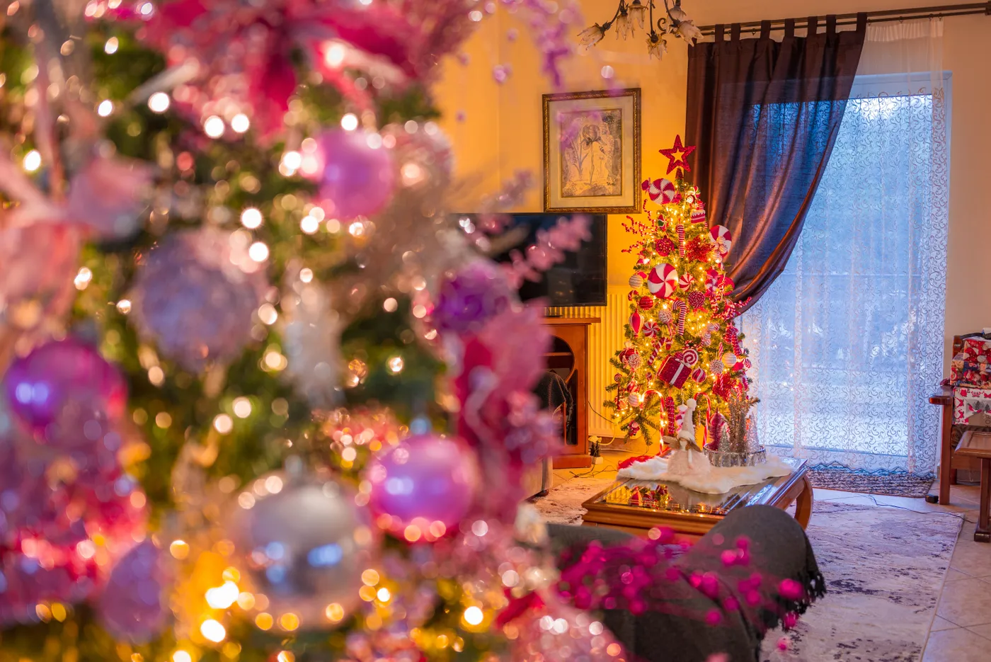 A warm, festive living room adorned with illuminated Christmas trees in pink and purple decorations.