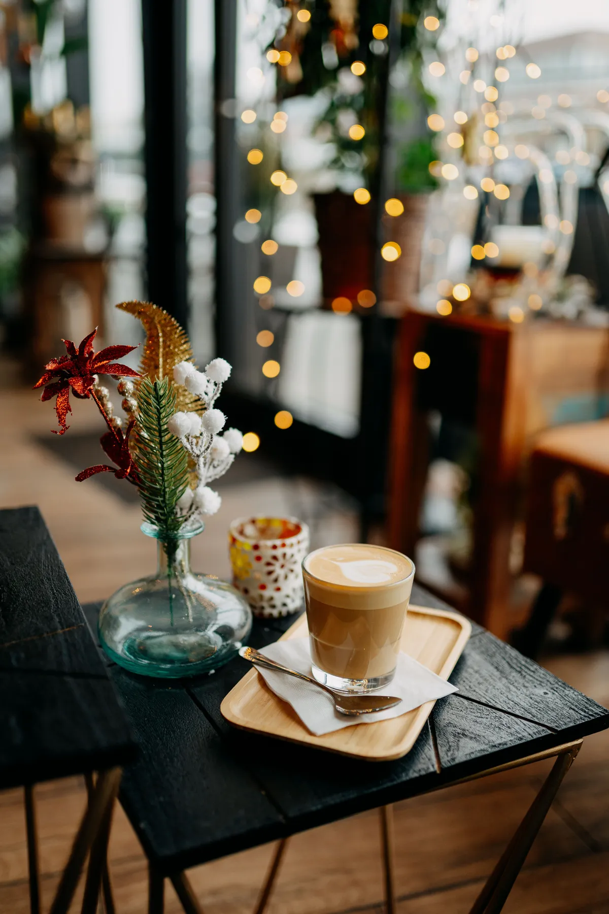 A warm latte on a wooden table in a cozy café with festive decor and lights.