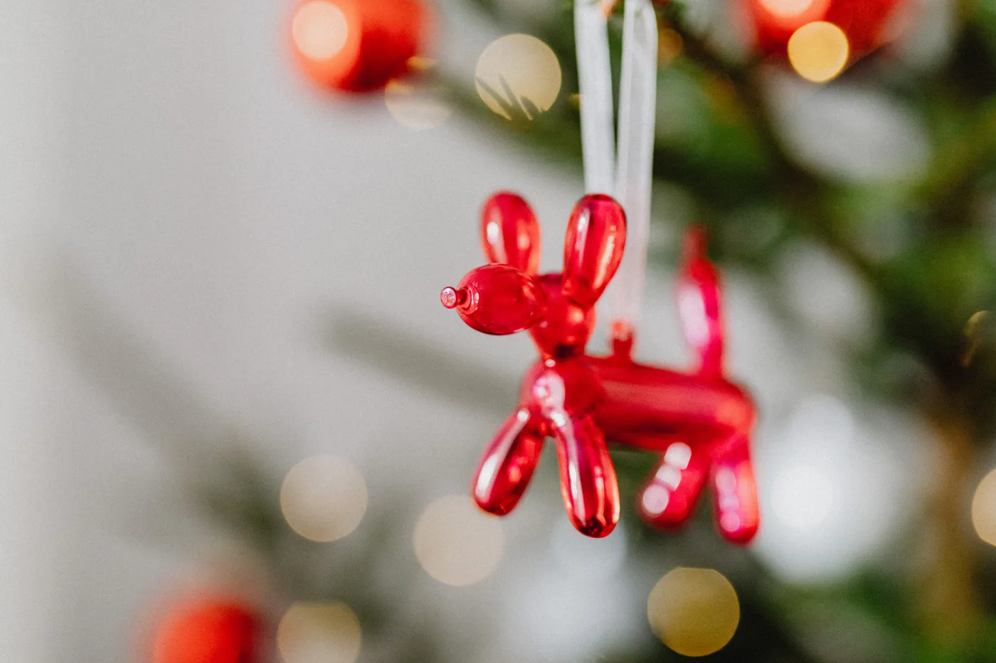 Bright red balloon dog ornament hanging on a Christmas tree, adding festive cheer.