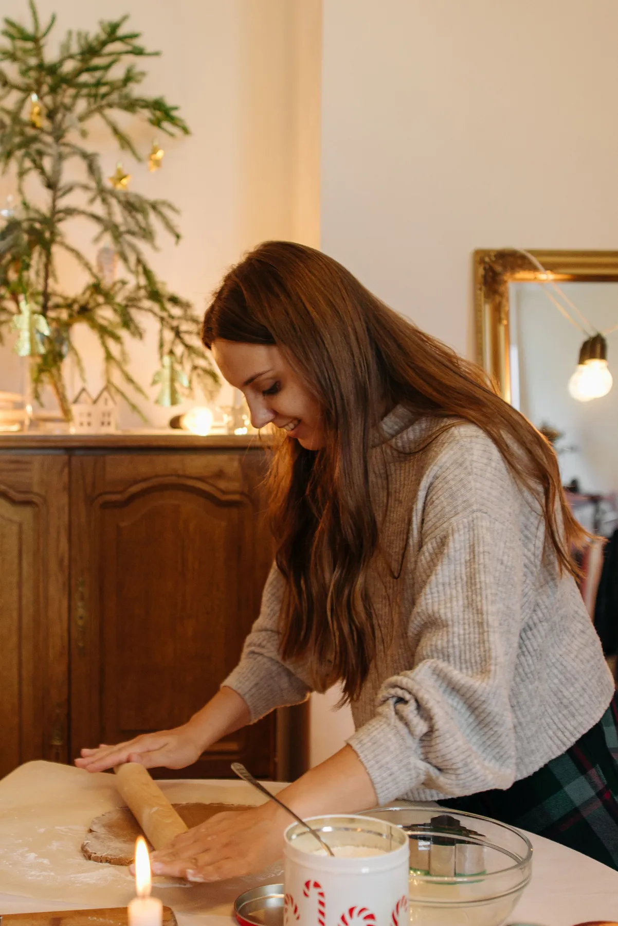 Caucasian woman rolling dough in a festive kitchen setting with Christmas decorations.