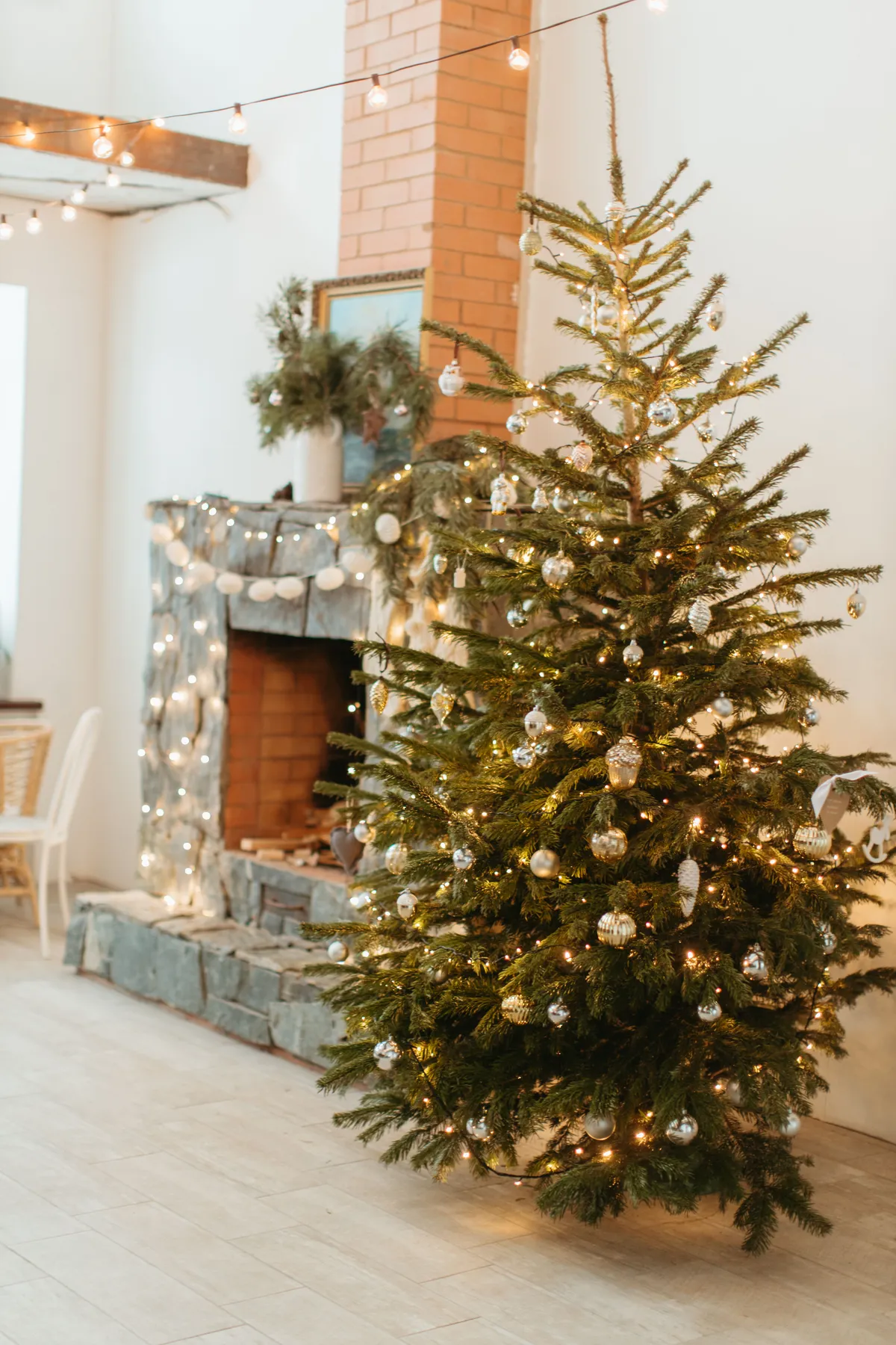 Charming Christmas tree adorned with lights and ornaments next to a festive fireplace in a cozy home setting.