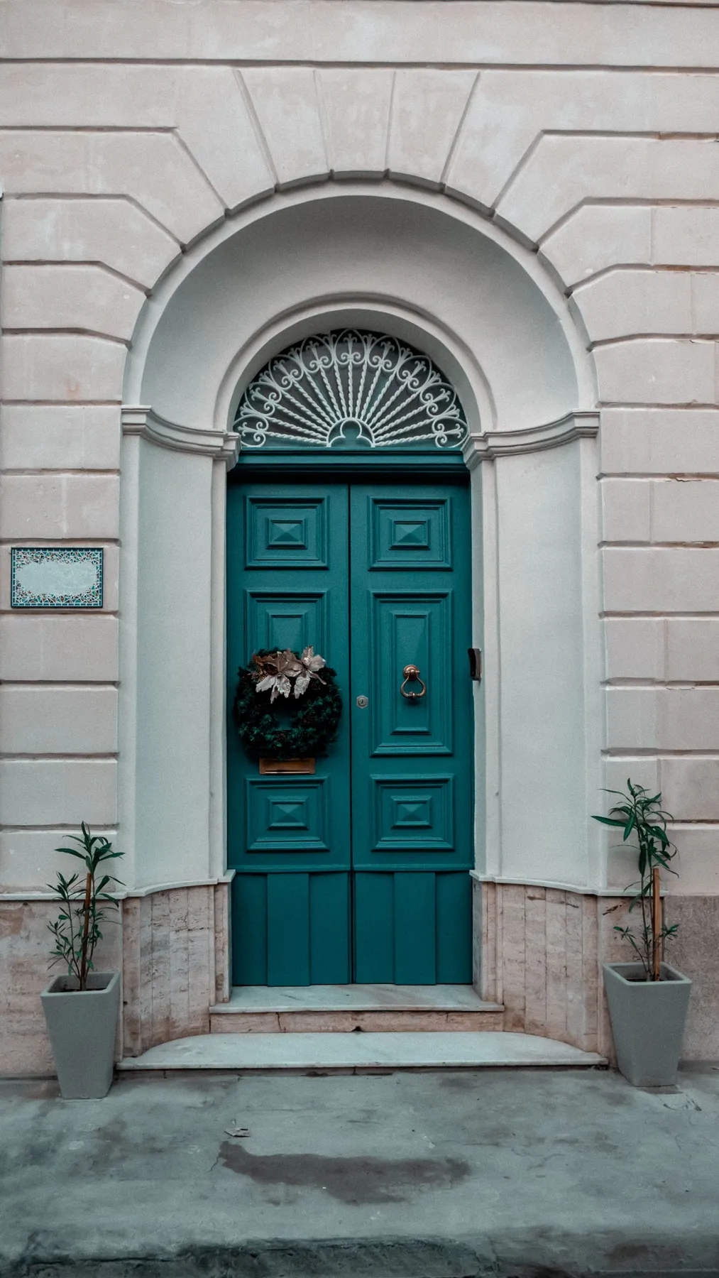 Charming doorway with teal door and festive wreath in classic European architecture.