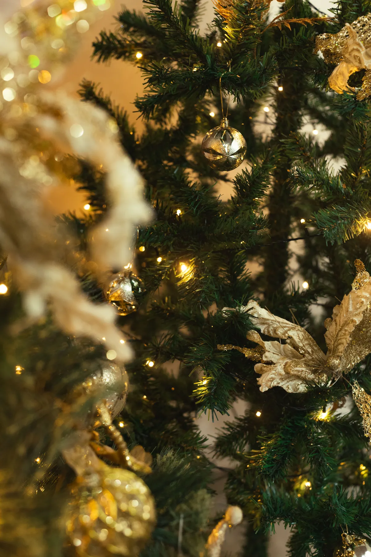 Close-up of a beautifully decorated Christmas tree with gold ornaments and warm lights.