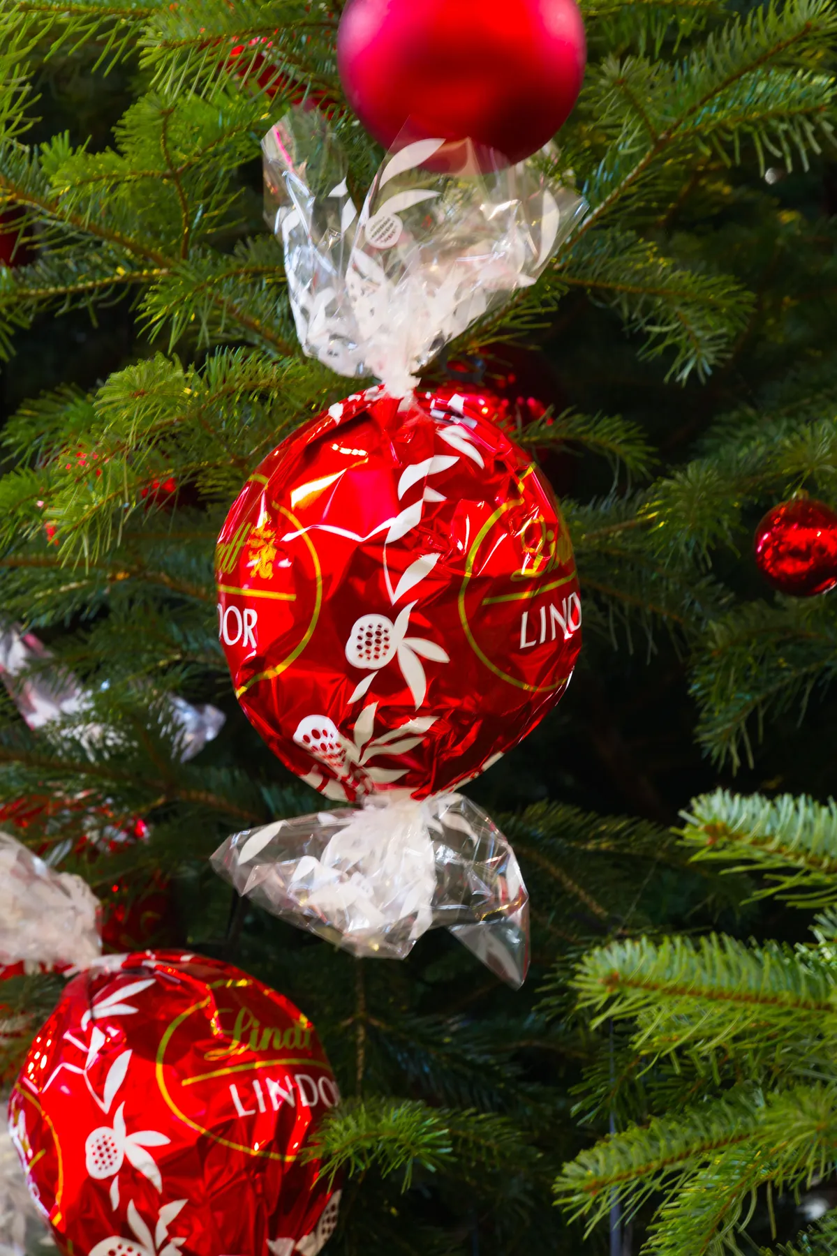 Close-up of a red Lindor candy ornament on a Christmas tree, capturing festive joy.