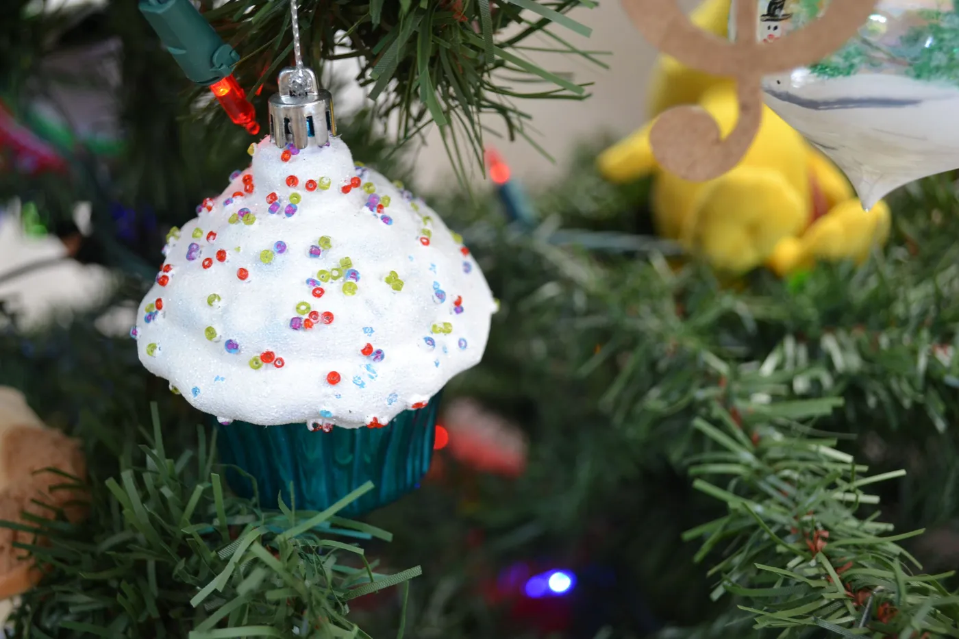 Colorful cupcake ornament with sprinkles hanging on a Christmas tree branch.