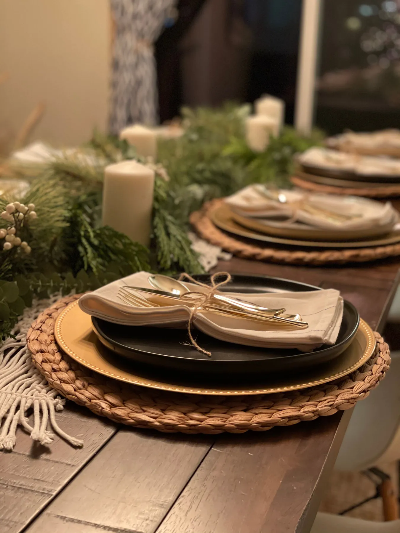 Cozy holiday dinner table setup with candles, greenery, and elegant tableware.
