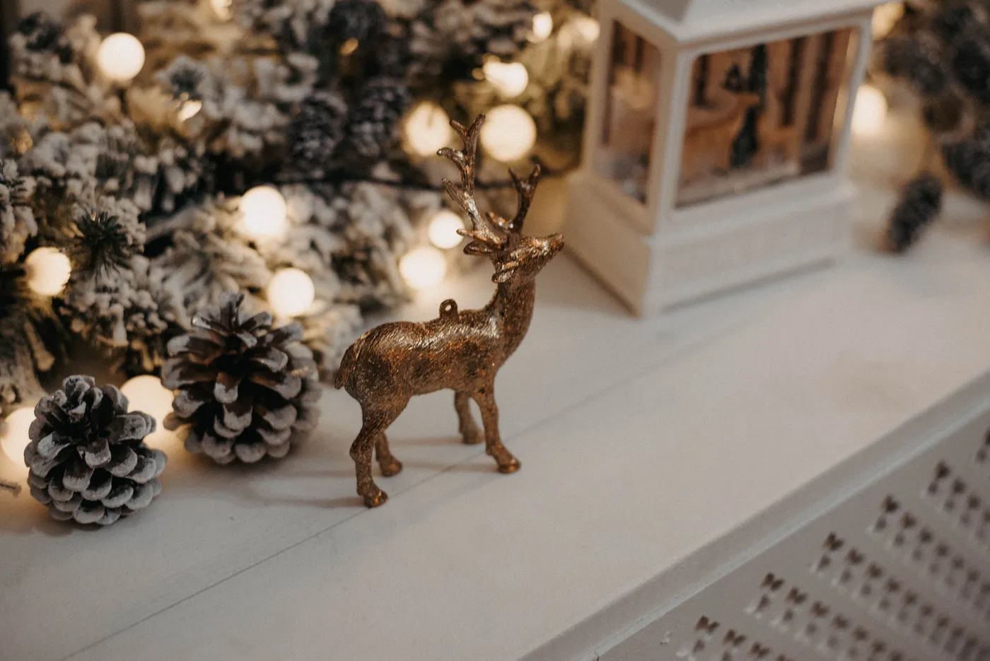 Cozy winter decor with pinecones, lights, and reindeer ornament on a mantel.
