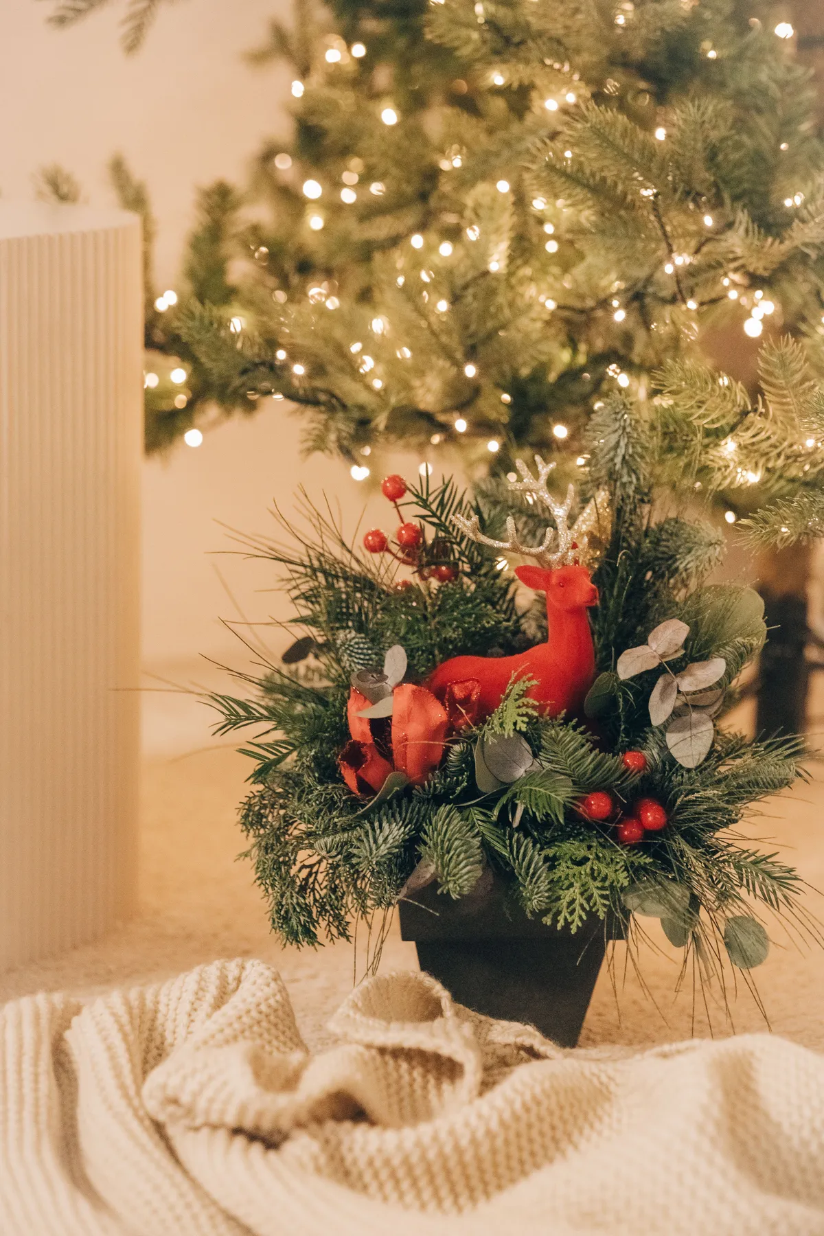 Elegant Christmas centerpiece featuring a red reindeer surrounded by green foliage and holiday decor.
