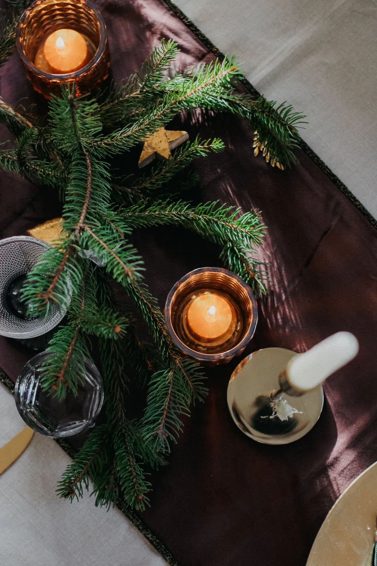 Elegant Christmas table setup with candles and evergreen branches for a festive ambiance.