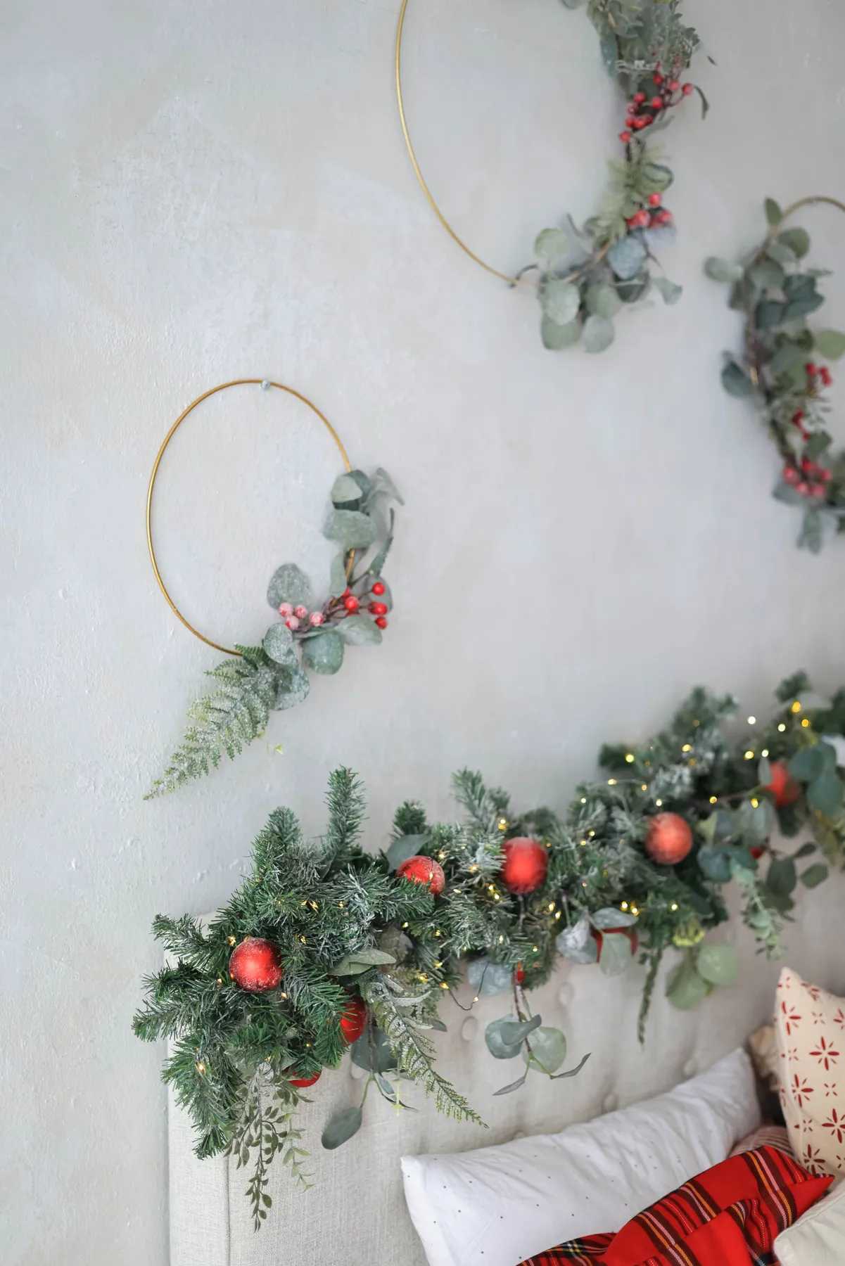 Elegant Christmas wreaths and garland with red accents on a white wall.