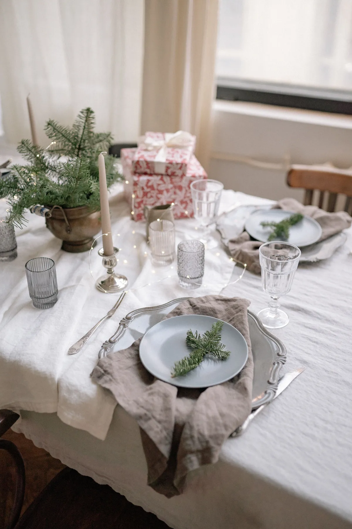 Festive dining table setup with elegant decorations, gifts, and greenery for a Christmas celebration.