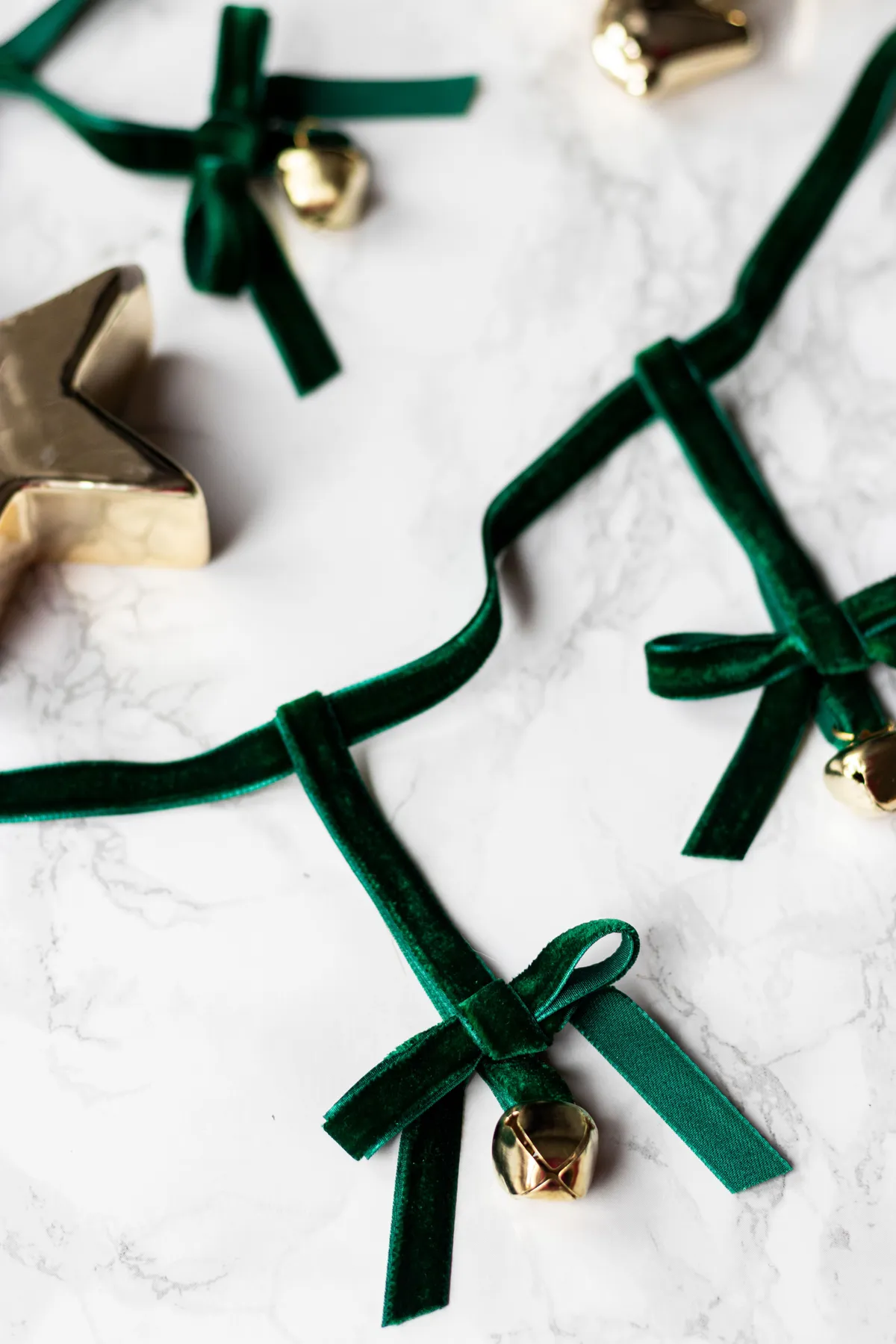 Festive gold star and jingle bells with green ribbons on marble background.