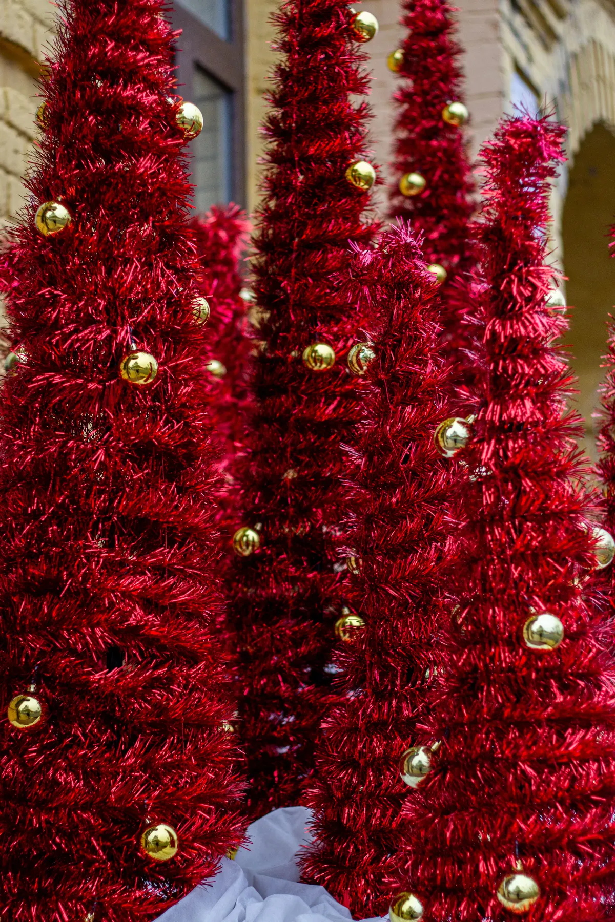 Festive red tinsel Christmas trees with sparkling gold ornaments in a holiday display.