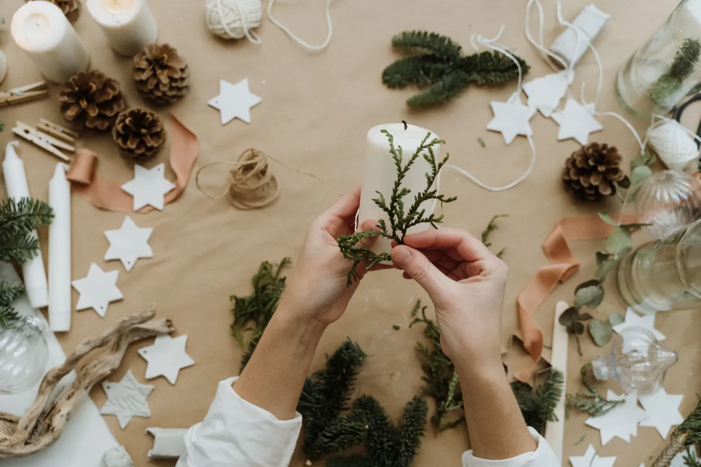 Hands decorating a candle with greenery for a cozy winter holiday setting.