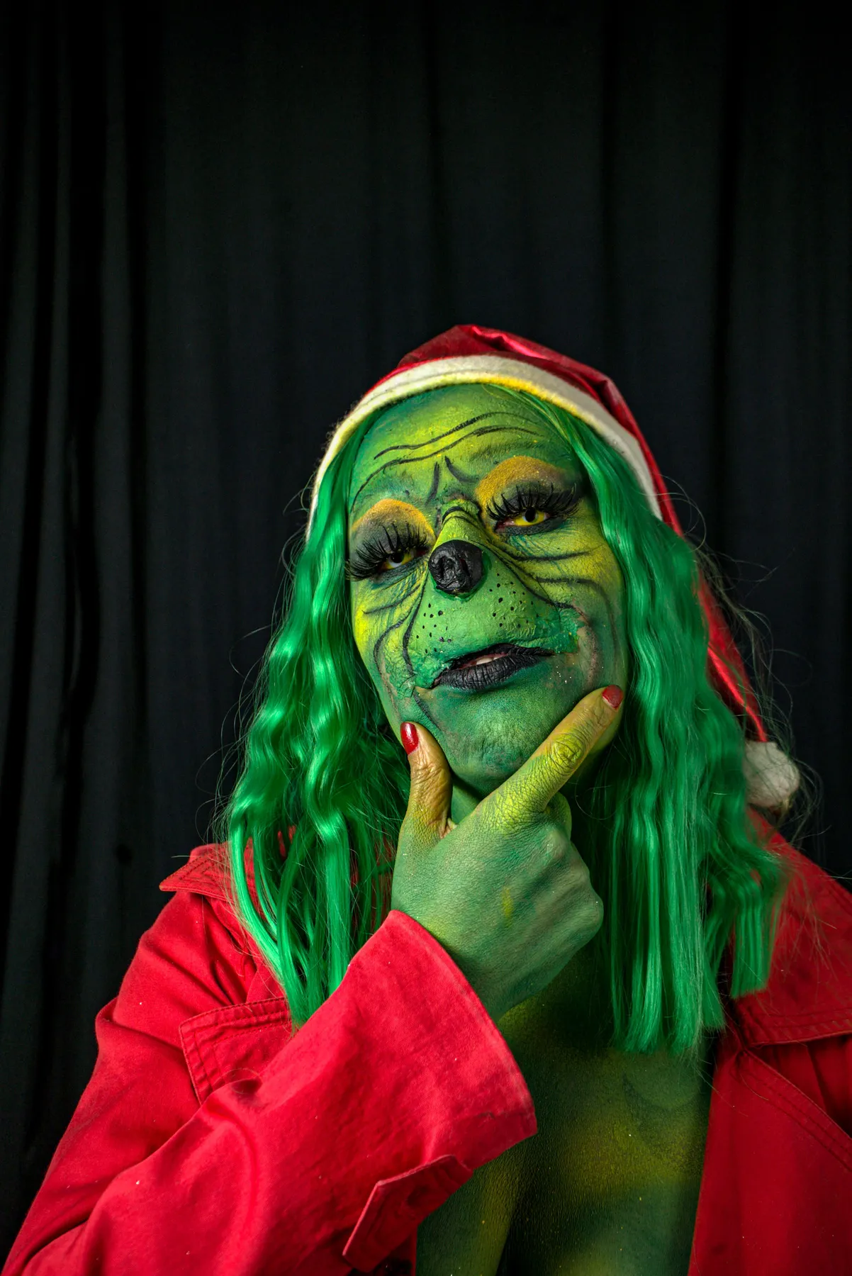 Person in a vivid Grinch costume with Santa hat posing thoughtfully.