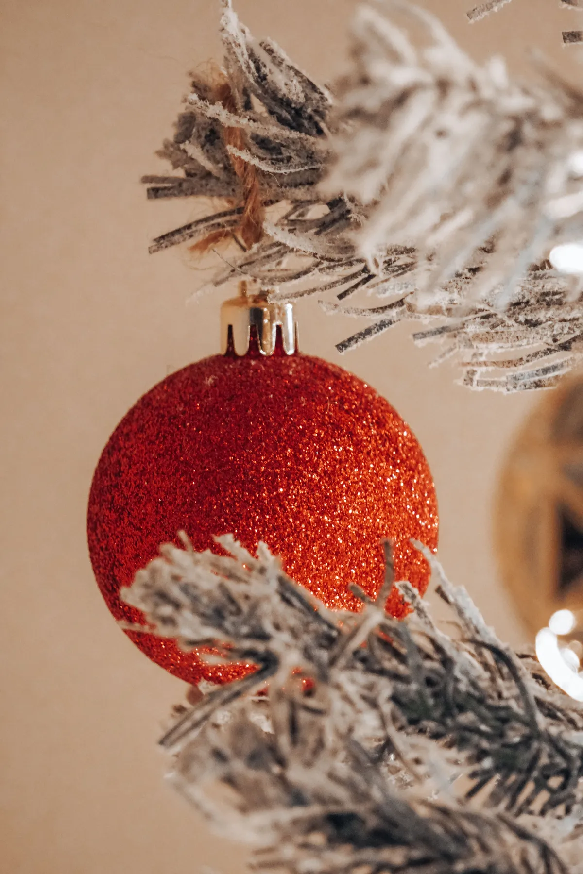 Red glittery Christmas ornament hanging on a frosted tree branch against a muted background, capturing festive elegance.