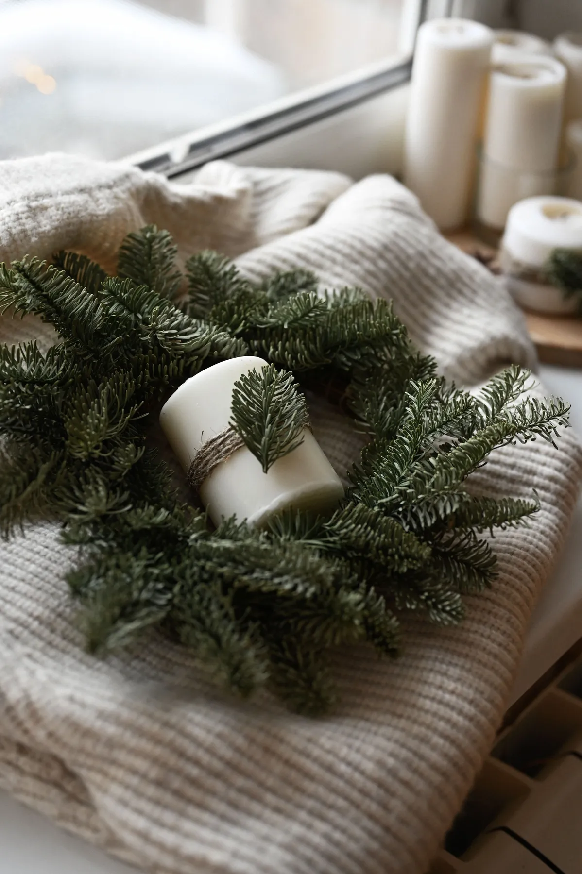 Rustic candle wrapped in a wreath by a window, evoking winter coziness.