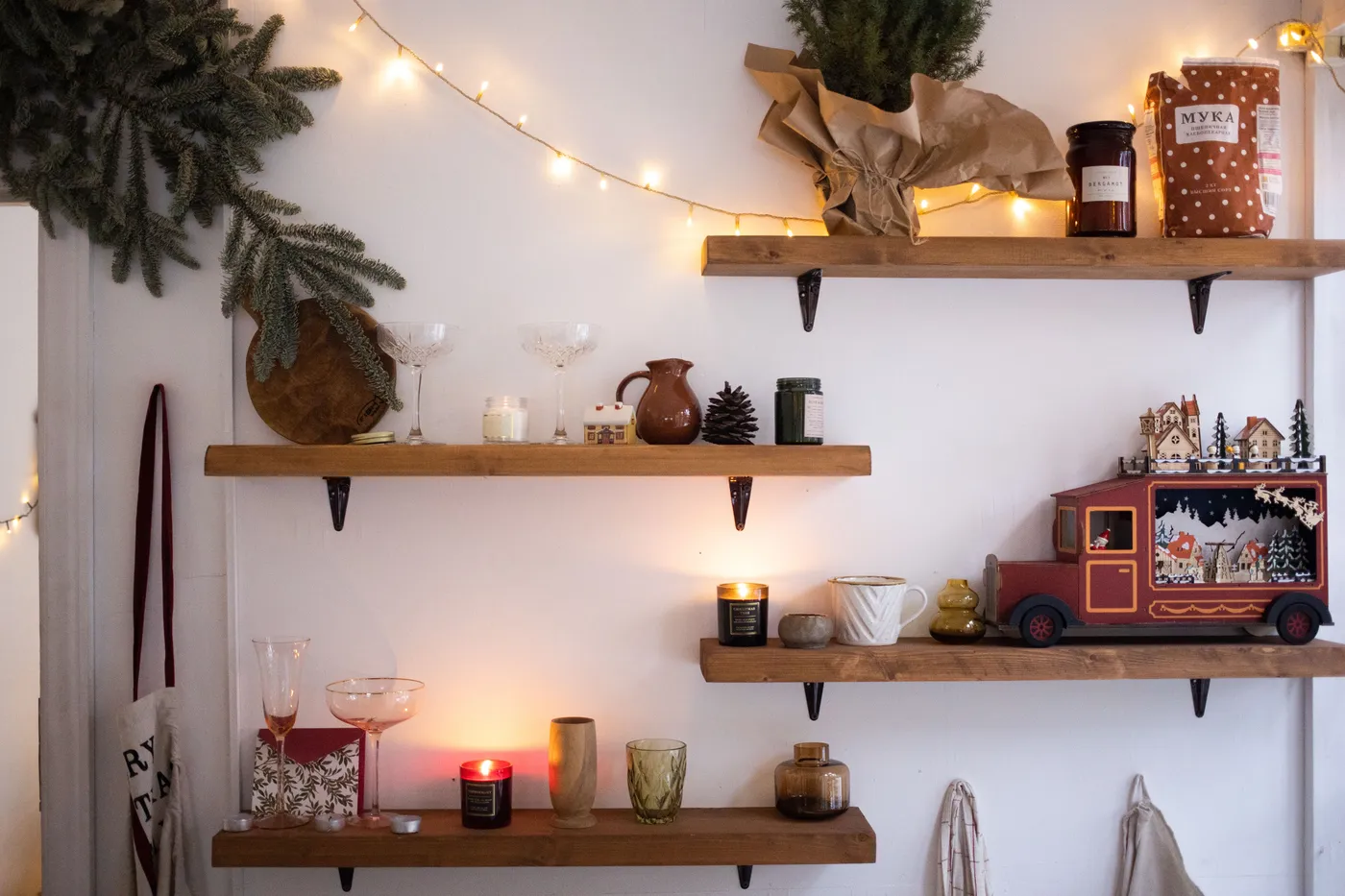 Warm Christmas scene with festive decorations and lights on wooden shelves indoors.