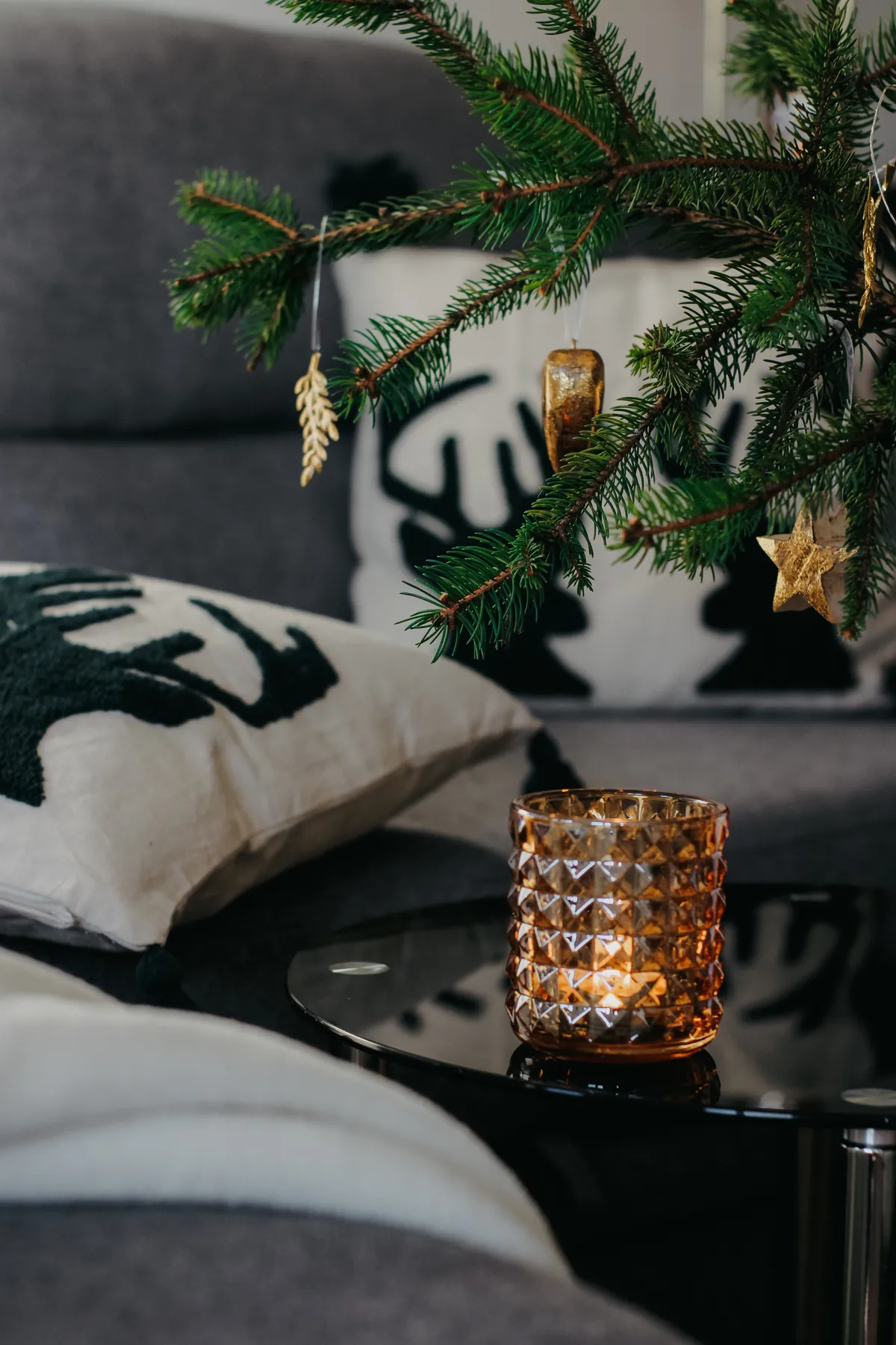 Warm living room scene with a burning candle, Christmas tree, and festive cushions.