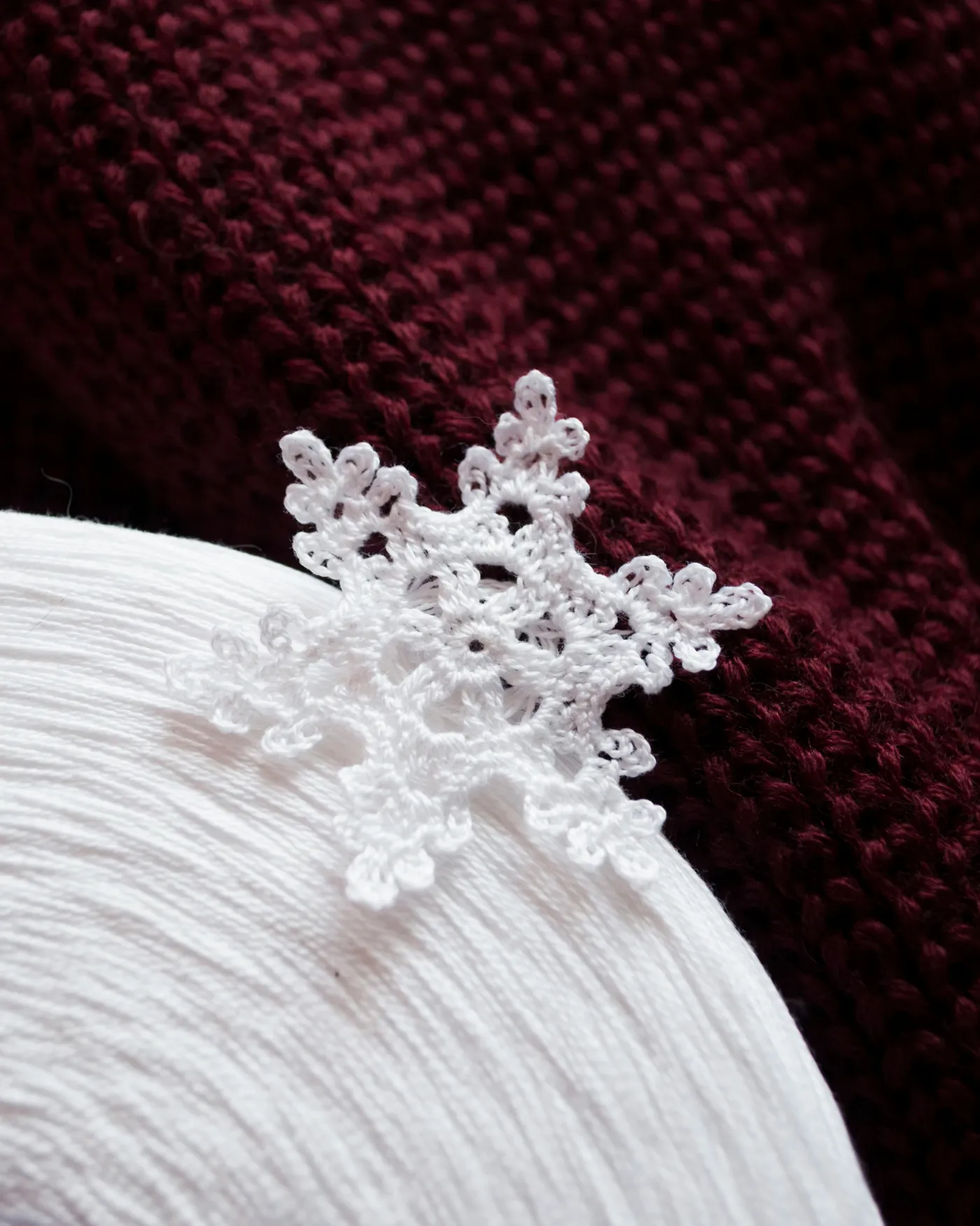 White crocheted snowflake on white yarn and burgundy knit